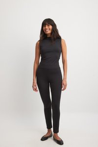 Melna topa un legingu komplekts, kas izgatavots no gludas, stiepjamas auduma. Iezīmēts ar augstu apkakli un pieguļošu dizainu, saskaņots ar melniem apaviem bez papēžiem.