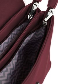 Bordó kabelka s dvěma zipovými oddíly. Interiér podšitý tkaninou se zigzagovým vzorem v šedé a bílé barvě. Stříbrné kovové doplňky.