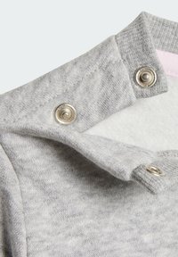 Prenda de algodón gris con una textura suave, que presenta un cuello doblado, broches a presión en tono plateado y un acento rosa en la parte inferior.