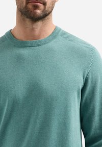 Turquoise trui gemaakt van zachte brei stof, met een ronde halslijn en geribbelde details op de kraag en schouders.