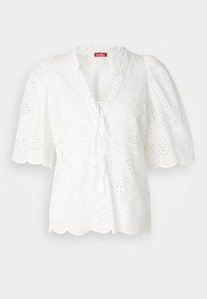 White blouse with puffed sleeves, eyelet fabric featuring floral and paisley patterns, scalloped hem, and a V-neckline with tie detail.