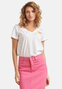 White cotton v-neck t-shirt featuring a small ice cream cone design. Paired with a bright pink denim skirt, showing a fitted silhouette.
