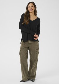 Maglione nero a v-neck con maniche lunghe, abbinato a pantaloni cargo larghi color olive con tasche laterali e una finitura testurizzata.