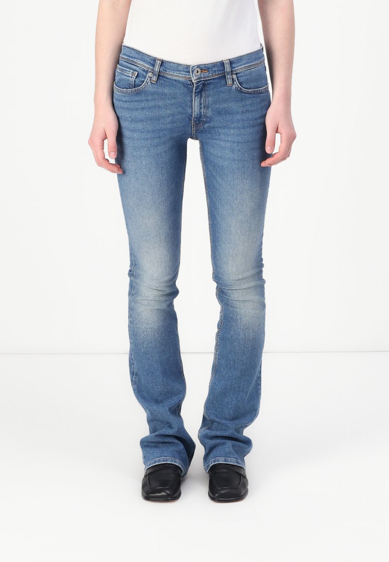 Jean en denim bleu avec une coupe ajustée, une texture délavée et des jambes légèrement évasées. Comprend des poches avant et une fermeture éclair avec un bouton.