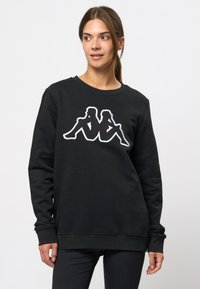 Zwarte sweatshirt van zachte stof met een witte geborduurde afbeelding van twee zittende figuren op de voorkant. Ronde halslijn en lange mouwen.