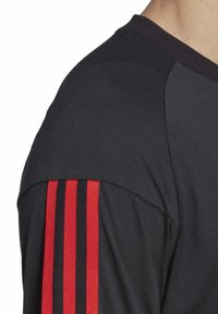 T-shirt de sport noir en tissu texturé ; présente des rayures rouges et noires sur l'épaule. Conception classique à col rond.