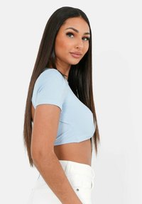 Lyseblå ribbet crop top med korte ærmer. Blusen har et tætsiddende design og en rund halsudskæring, parret med hvide højhalsede jeans.