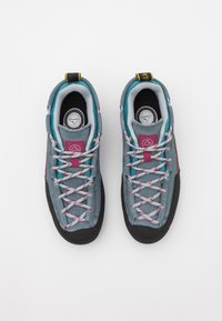 Pelēkie zamšādie sporta apavi ar tirkīza akcentiem, melna gumijas zole, rozā šņorēšanas cilpas un daudzkrāsainas šņorītes. Iekšējā daļā ir mīksts apkakles apvalks un logotips uz mēles.