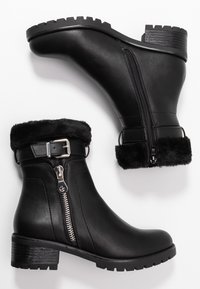 Bottes basses en cuir noir avec bord en fourrure texturée, fermetures éclair latérales et boucles argentées. Dotées d'un talon épais et texturé pour une meilleure adhérence.