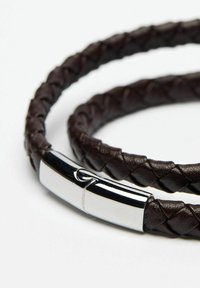 Brun flätad läderarmband med ett silvermetallspänne, med en slät yta och en elegant, flexibel design.