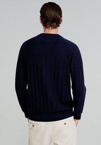 Granatowy sweter z dzianiny z pionowymi prążkami, okrągłym dekoltem oraz prążkowanymi mankietami i dołem. Model pokazany od tyłu.