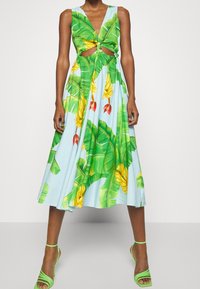 En ærmeløs, lyseblå kjole med et tropisk print af grønne bananblade og gule bananer, med udskæringer og en svævende silhuet.