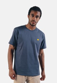 Krátký rukáv, námořnická tričko z měkké bavlny s kulatým výstřihem a malým žlutým logem slona na hrudi. Hladká textura a jednoduchý design.