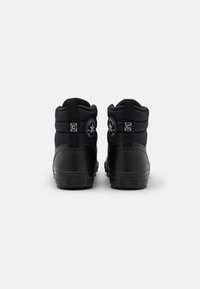 Een paar zwarte high-top Converse All Star sneakers gezien vanaf de achterkant op een effen witte achtergrond.