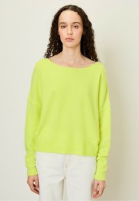 Heldere limoengroene oversized trui met een wijde hals, lange mouwen en geribbelde manchetten, in combinatie met witte denim broek.