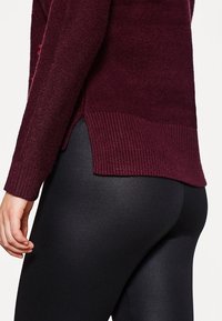 Burgundowy sweter z dzianiny z prążkowanym wykończeniem, zestawiony z czarnymi legginsami. Sweter ma boczne rozcięcia, które dodają stylu i komfortu.