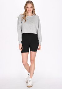 Grå kortad sweatshirt med långa ärmar i kombination med svarta stretchshorts. Modellen bär vita hög- eller sneakers med beige detaljer.