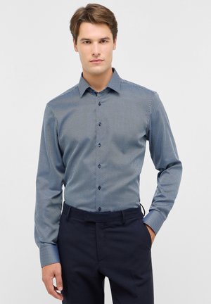 Blauw gestreept overhemden met een knoopsluiting aan de voorkant, een gespreide kraag, lange mouwen en contrasterende donkere knopen, gecombineerd met donkere broeken.