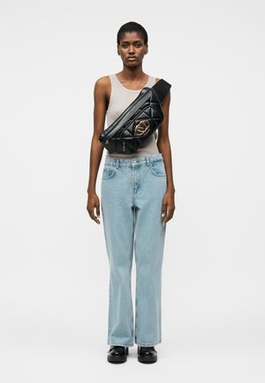 Kvinde iført en beige tanktop, lyseblå jeans, sorte sko og en sort quiltet crossbodytaske med guldhardware.