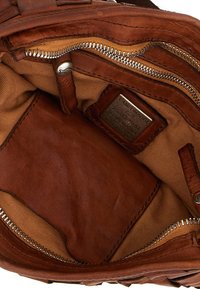 Interno di borsa in pelle marrone con rivestimento in tela color cuoio, molteplici tasche con zip e una targhetta metallica del marchio. Texture liscia e design pratico.