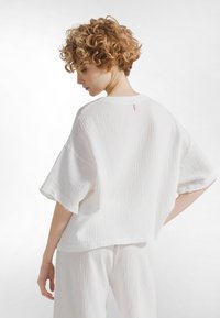 Witte, gestructureerde katoenen top met een losse pasvorm en verlaagde schouders. Opvallende naad aan de achterkant en rafelige mouwenranden. Gecombineerd met bijpassende broek.