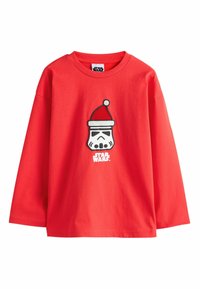 Červené bavlněné tričko s dlouhým rukávem, které zobrazuje grafiku stormtroopera nosícího vánoční čepici, s nápisem "STAR WARS" pod designem.
