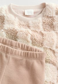 Jasnoróżowy polarowy top z teksturowanymi kwadratami oraz pasującymi beżowymi spodniami z elastyczną talią. Metka informuje "NEXT baby".