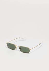 Gafas de sol con montura dorada y lentes ovalados de color verde oscuro. Patillas delgadas de alambre con acentos transparentes. Diseño minimalista y construcción ligera.