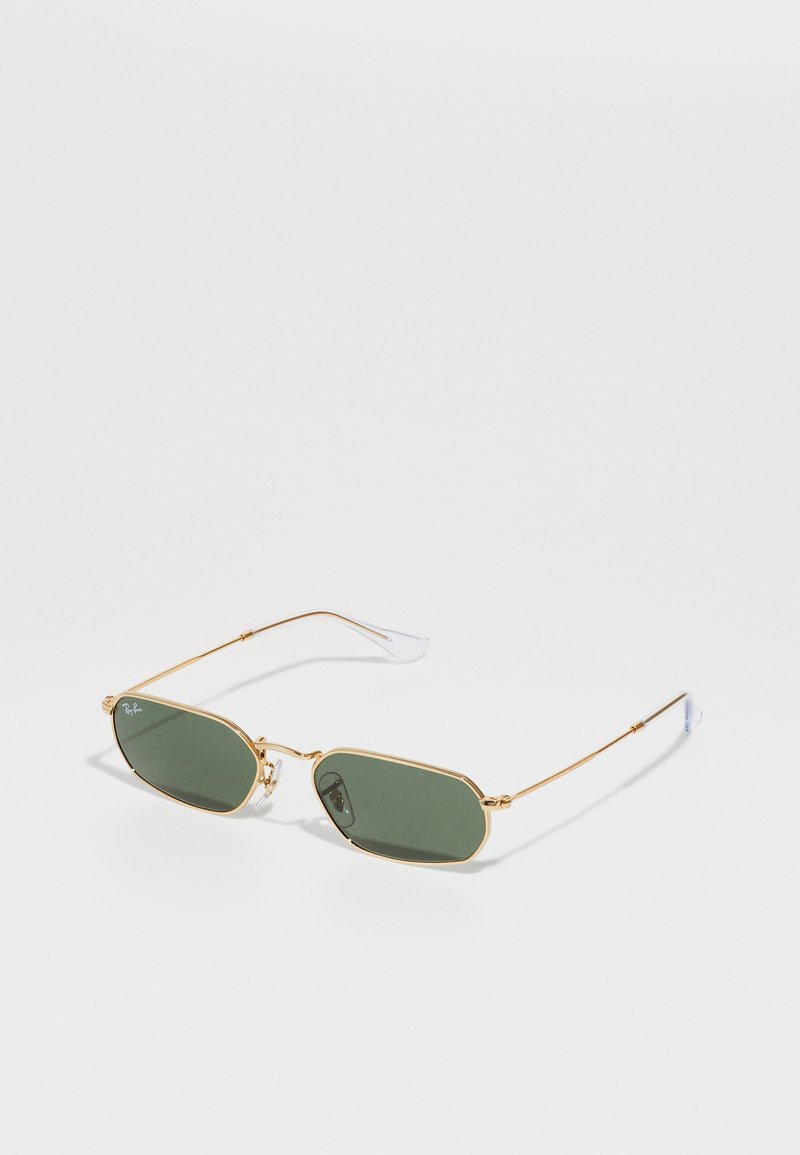 Gafas de sol con montura dorada y lentes ovalados de color verde oscuro. Patillas delgadas de alambre con acentos transparentes. Diseño minimalista y construcción ligera.