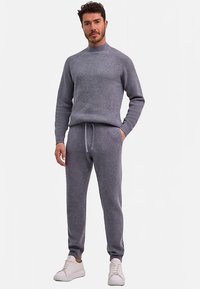 Maglione grigio a maglia con collo alto e texture a coste, abbinato a pantaloni jogger coordinati con cintura elastica. Scarpe da ginnastica bianche.