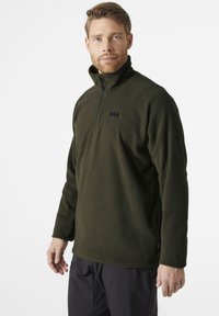 Sudadera de forro polar en verde oscuro con media cremallera, presenta un pequeño logo negro en el pecho y mangas largas. El material parece suave y con textura.