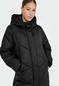 Cappotto puffer nero con cappuccio, imbottitura orizzontale e a chevron, tasche con zip e coulisse regolabili per una vestibilità sicura.