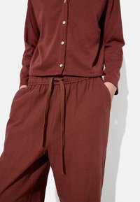 Burgundowy zestaw odzieży domowej składający się z koszuli z guzikiem o okrągłym dole oraz spodni z troczkiem. Miękki materiał o luźnym kroju i boczne kieszenie.