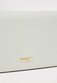 White textured wallet with a smooth finish, featuring a gold logo plate and contrasting stitching along the edges.
