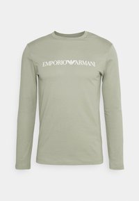 Langärmliges, salbeigrünes Hemd mit weißem "Emporio Armani"-Logo und Adleremblem, zentriert auf der Brust, einfarbiger Hintergrund.