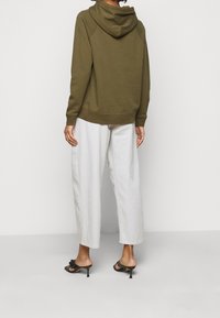 Olijfgroene hoodie met een buidelzak, ribgebreide manchetten en onderrand, gecombineerd met wijde witte broek en zwarte hoge hakken.