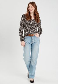 Blouse noire à manches longues avec un motif floral beige, associée à un jean droit bleu clair et une ceinture marron. Des chaussures noires complètent la tenue.