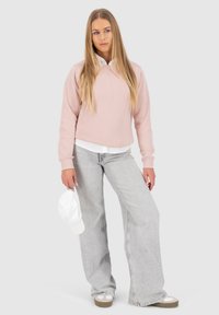 Felpa rosa chiaro con una vestibilità rilassata, indossata sopra una camicia bianca con colletto. Abbinata a jeans a vita alta grigi chiari a gamba larga e un cappellino bianco.