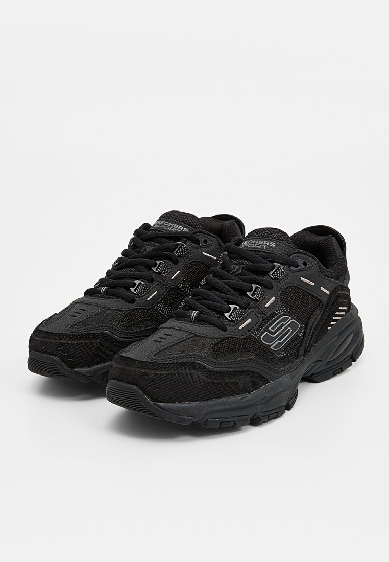 Baskets de sport noires avec un dessus en maille et en synthétique, des détails texturés, un système de laçage, un col rembourré et un logo reconnaissable sur le côté.