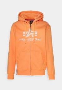 Felpa arancione con zip, realizzata in tessuto morbido, dotata di cappuccio regolabile, tasche frontali e logo bianco sul petto.