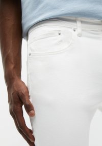 Witte denim jeans met een gladde textuur en een slim fit, met een klein voorkantvakje en metalen accenten. Gestyled met een lichtblauw overhemd.