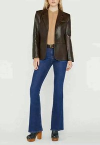 Blazer in pelle marrone sopra un maglione beige a coste, abbinato a jeans svasati blu e scarpe con piattaforma nere con tacco in legno.