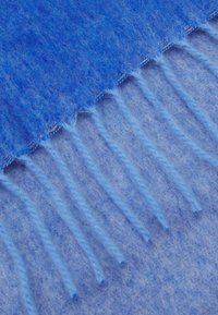 Couverture en laine bleue avec une texture douce, présentant un dégradé du bleu foncé au bleu clair, finie par des bords fringés.