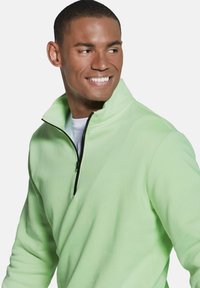 Light green fleece pullover with a high collar, featuring a black zipper and a soft, textured fabric. Design is modern and fitted.