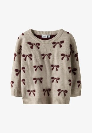 Beżowy sweter z okrągłym dekoltem, posiadający teksturowany materiał, wzory w czerwone kokardy oraz prążkowane mankiety i dół. Idealny na codzienne noszenie.