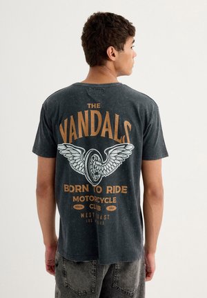 Camiseta negra de manga corta con un gran diseño impreso en la parte posterior que incluye el texto "THE VANDALS", un gráfico de una rueda con alas y detalles del club.