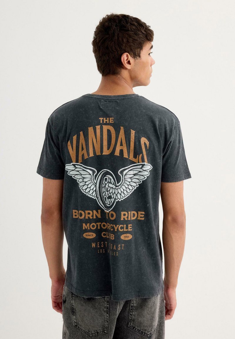 Camiseta negra de manga corta con un gran diseño impreso en la parte posterior que incluye el texto "THE VANDALS", un gráfico de una rueda con alas y detalles del club.