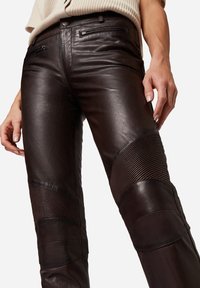 Bruine leren broeken met een slim fit, gedetailleerde stiksels, geribbelde accenten op de knieën en voorzakken met ritssluiting.