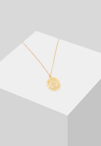 Collar con colgante de color dorado que presenta un intrincado diseño de corte floral, suspendido de una fina cadena. Presenta un acabado suave y detalles delicados.