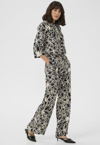 Black and cream floral-patterned matching set with a collared shirt and wide-leg pants. The fabric has a smooth texture and relaxed fit.